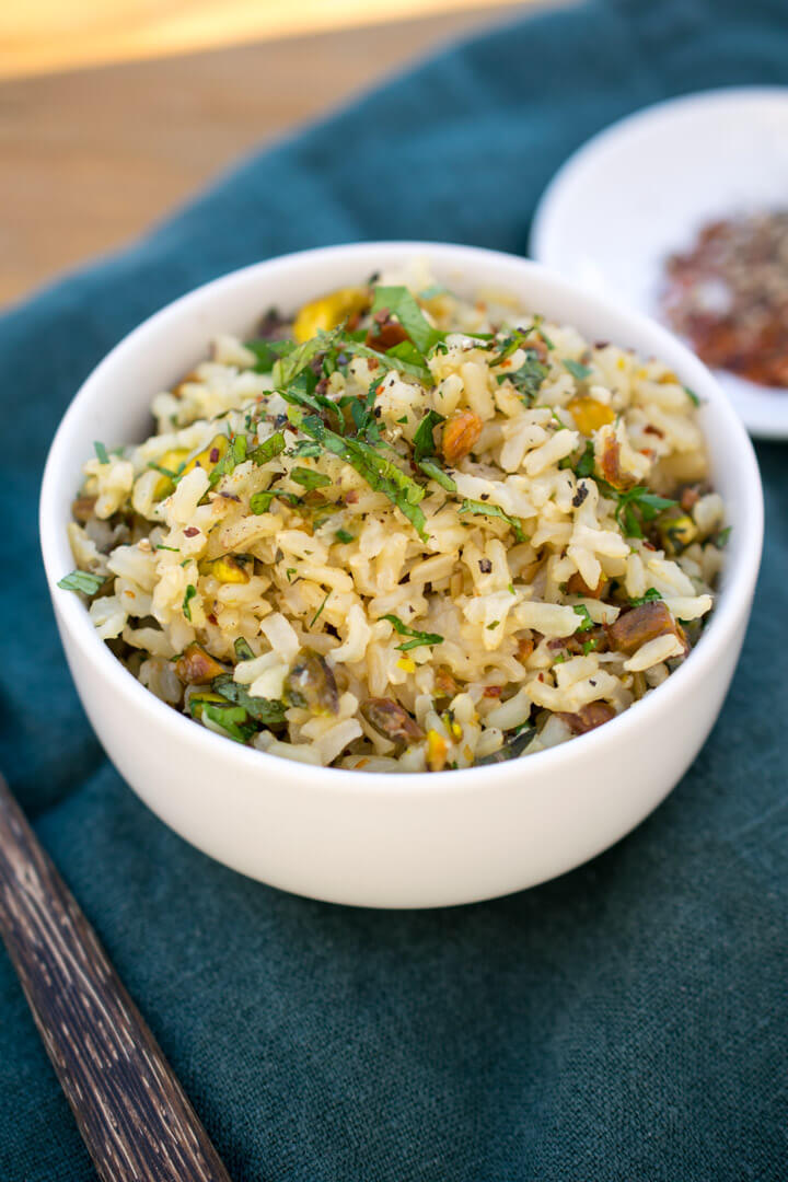 Baked brown rice pilaf in a white ceramic bowl garnished with thinly sliced parsley and mint 